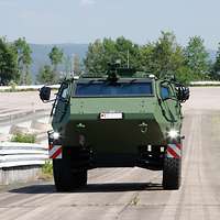 Frontansicht des grünen Patria-Radpanzers, der sich auf einer Fahrbahn befindet.