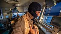 Ein Soldat mit einer Flammenschutzhaube auf der Brücke von einem Schiff der Deutschen Marine