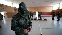 Ein Soldat steht in einer ABC-Ausrüstung in einem großen Raum.