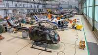 In einer großen Halle stehen mehrere Hubschrauber und Flugzeuge.