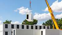 Eine Reihe übereinandergestapelter Container, davor ein Kran, der einen weiteren Container platziert.