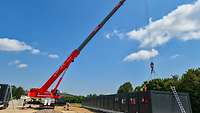 Ein roter Kran stellt Container auf eine Bodenplatte.