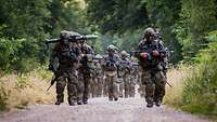 Soldaten marschieren in einer Gruppe mit Ausrüstung einen Waldweg entlang