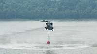Ein Hubschrauber vom Typ CH-53 nimmt Löschwasser aus einem See auf