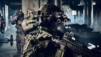 Drei Soldaten laufen mit Nachtsichtbrillen und Waffen nach allen Seiten sichernd durch ein Gebäude.