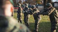 Vier Soldaten mit Sturmgewehr stehen auf einer Wiese nebeneinander. 