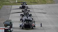 Vier Militärhubschrauber stehen teils mit eigeklappten Rotoren hintereinander