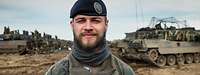 Soldat im Porträt im Hintergrund Panzer auf aufgewühltem Feld