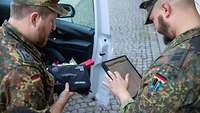 Zwei Soldaten stehen vor einem Fahrzeug und schauen auf ein Tablet.