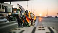 Ein Techniker rangiert ein Arbeitsgerät auf dem Flugvorfeld im Sonnenuntergang.