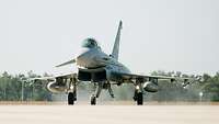 Ein Eurofighter rollt mit eingeschalteten Landelichtern in der Sonne auf der Startbahn.