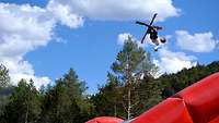 Ein Sportler auf Ski springt in sommerlicher Kulisse auf einem großen Airbag.