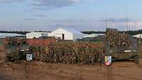 Gruppenfoto von mehreren Soldaten, die zwischen zwei Gefechtsfahrzeugen stehen.