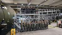 Ein neuer Azubijahrgang steht in Formation neben einer C-160 Transall in der Ausbildungshalle.