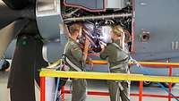 Am geöffneten Triebwerk des A400M stehen ein Techniker und eine Technikerin und arbeiten.