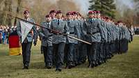 Eine Gruppe von Soldaten marschiert über eine Wiese. Eine Soldatin an der Spitze trägt eine Fahne.