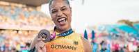 Eine Sportlerin hält eine Bronze-Medaille in die Kamera und freut sich.
