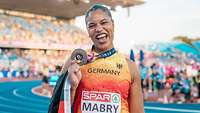 Eine Sportlerin hält eine Bronze-Medaille in die Kamera und freut sich.