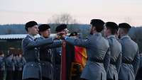 Sechs Soldaten legen jeweils eine Hand auf die abgesenkte Truppenfahne und sprechen.
