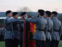 Sechs Soldaten legen jeweils eine Hand auf die abgesenkte Truppenfahne und sprechen.
