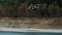 Ein Hubschrauber nimmt Wasser mit einem Löschwasserbehälter auf.