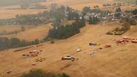 Luftbild von einem Feld, auf dem mehrere Fahrzeuge von Einsatzkräften stehen.