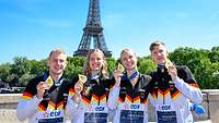 Vier junge Sportler posieren mit ihren Goldmedaillen, im Hintergrund der Eifelturm in Paris.
