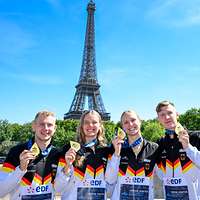 Vier junge Sportler posieren mit ihren Goldmedaillen, im Hintergrund der Eifelturm in Paris.
