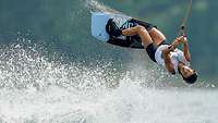 Frau springt im Wasser auf einem Wakeboard stehend.