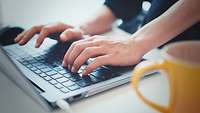 Hände tippen auf der Tastatur eines Laptops.