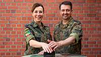 Eine Soldatin und ein Soldat drücken einen roten Buzzer.