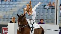 Eine Reitsportlerin führt eine Pose auf dem Rücken eines Pferdes aus.