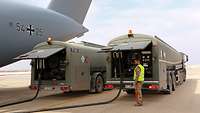 Ein Soldat mit Warnweste steht vor zwei Betankungswagen neben dem Heck eines Transportflugzeugs.