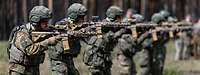 Mehrere Soldaten stehen im Gelände nebeneinander mit dem Gewehr G95 im Anschlag.