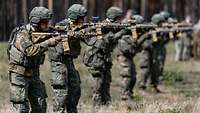 Mehrere Soldaten stehen im Gelände nebeneinander mit dem Gewehr G95 im Anschlag.