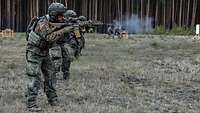 Mehrere Soldaten stehen in einer Reihe nebeneinander und schießen mit dem Gewehr G95 im Gelände.