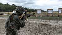 Ein Soldat zielt mit dem Gewehr G95 auf eine Zielscheibe, die im Gelände steht.