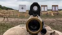Nahaufnahme vom Zielfernrohr und Visier des Gewehr G95. Dahinter stehen Zielscheiben im Gelände.