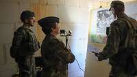 Eine Soldatin und zwei Soldaten stehen in einem dunklen Raum und blicken auf eine beleuchtete Karte.