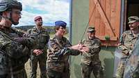 Fünf Soldatinnen und Soldaten stehen vor einem grünen Haus mit Fensterläden und sprechen miteinander.
