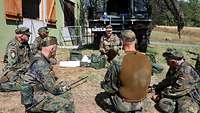 Soldaten sitzen in einem Kreis zusammen und bedienen verschiedene technische Geräte.