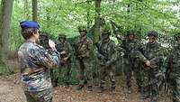 Eine Soldatin spricht zur Soldaten die in einer Linie im Wald stehen.