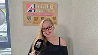 Eine Frau mit Mikrofon in der Hand steht vor einem Schild mit der Aufschrift „Radio Andernach“.