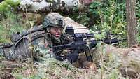 Ein Soldat mit Helm und Tarnschminke liegt mit seinem Gewehr in einer Stellung.