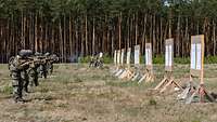 Soldaten stehen im Gelände nebeneinander in Reihe und schießen mit dem Gewehr G95 auf Zielscheiben.