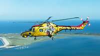 Ein Hubschrauber vom Typ Sea Lynx mit Sonderlackierung fliegt über ein Gewässer.