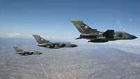  Drei deutsche Tornado-Kampfflugzeuge fliegen in enger Formation über einer trockenen, gebirgigen Landschaft.