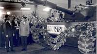 Ein Panzer mit der Aufschrift „Leopard“ und viele Besucher stehen in einer Werkhalle.