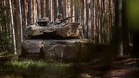 Ein Kampfpanzer vom Typ Leopard fährt durch das waldige Gelände.