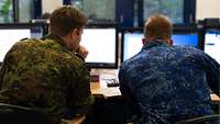Ein deutscher und ein niederländischer Soldat schauen auf einen Bildschirm.